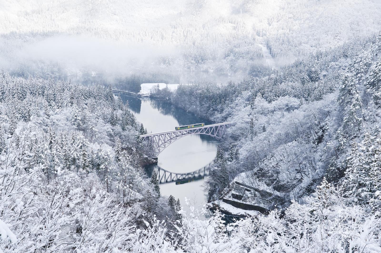 雪で白く覆われた山々の森と渓谷に架かる鋼鉄製の鉄道橋、列車が通過する冬景色