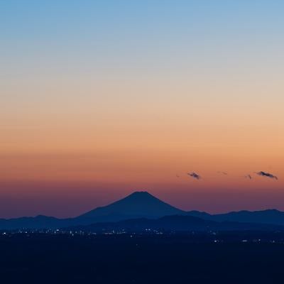 オレンジ色の夕焼けに浮かぶ富士山のシルエット、手前に町の灯りの写真