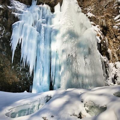 青白く凍った氷柱が幾重にも積み重なる日光の庵滝の氷瀑の写真