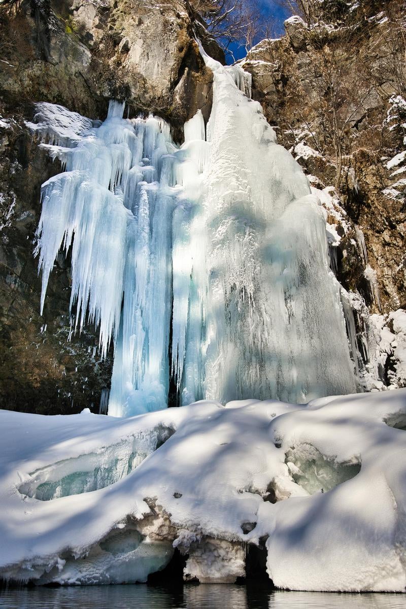 青白く凍った氷柱が幾重にも積み重なる日光の庵滝の氷瀑の写真