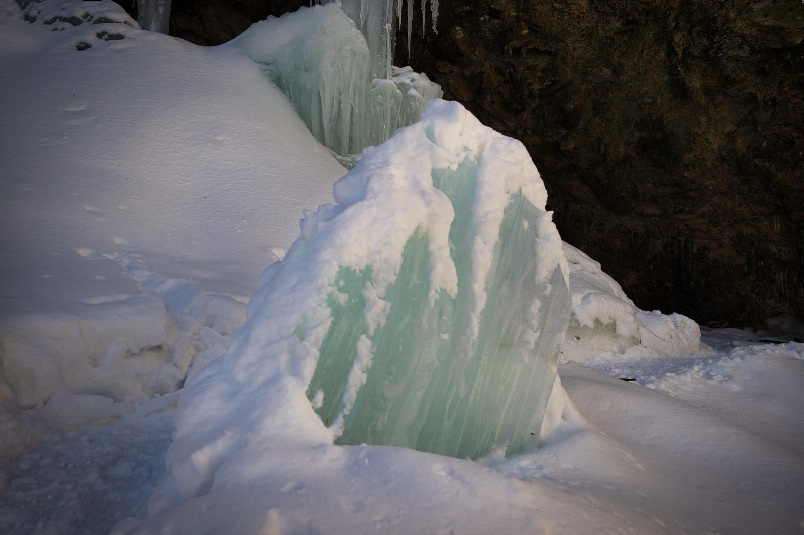 白い雪に覆われた地面から、緑と白に凍った大きな氷柱が積み重なって立つ冬の滝の景観
