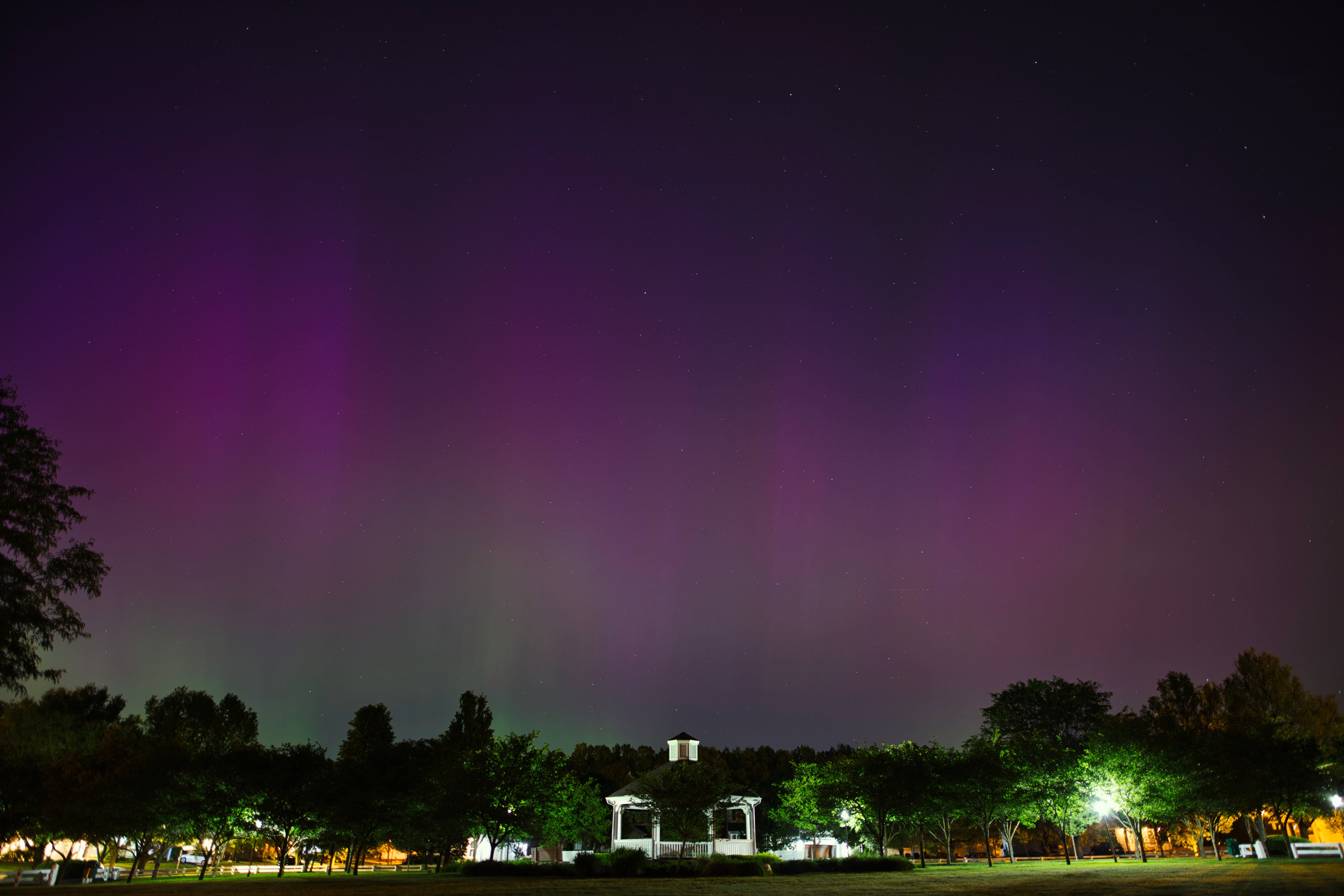 夜空に広がる紫色のオーロラと公園のガゼボの写真
