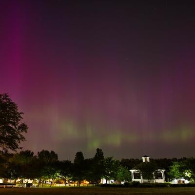 公園のガゼボを照らすピンク色のオーロラと星空の写真