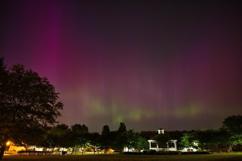 公園のガゼボを照らすピンク色のオーロラと星空