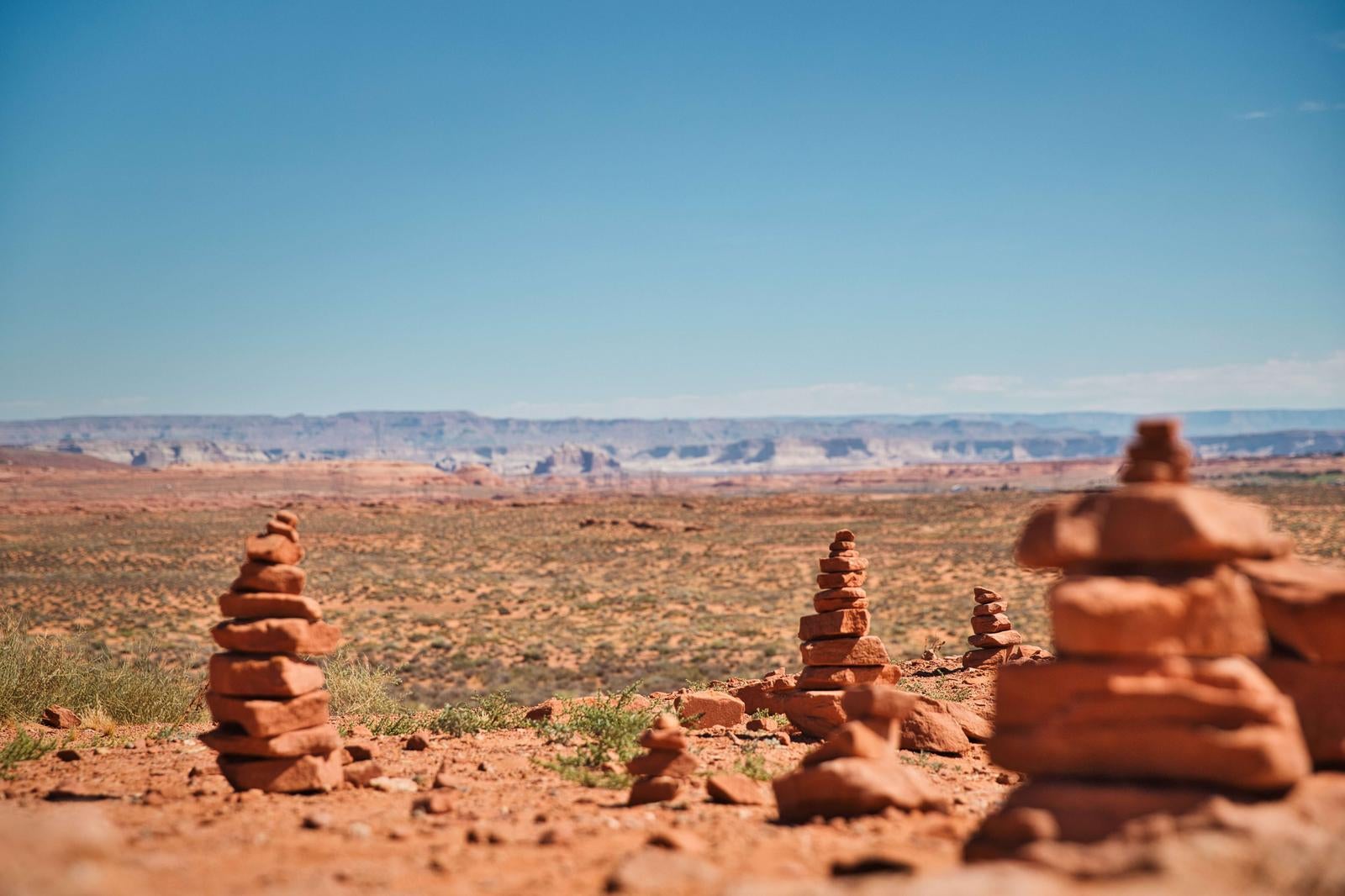 ブライスキャニオンの赤茶色い大地に積み上げられたケルン（石積み）が複数立ち並び、奥に台地状の岩山が見える砂漠風景