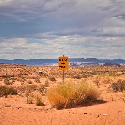 砂漠の荒野に立つ「STAY ON TRAIL」と山々の風景の写真