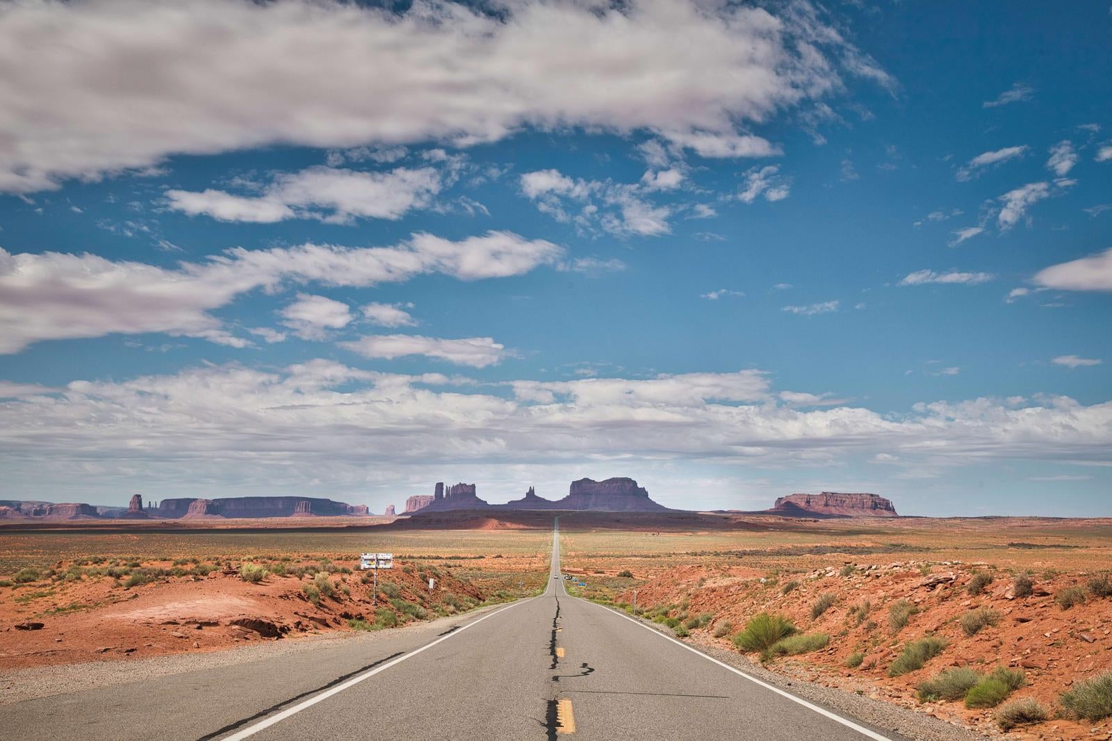 モニュメントバレーへ続く一直線の道路。左右の砂漠に赤褐色の岩山が見える