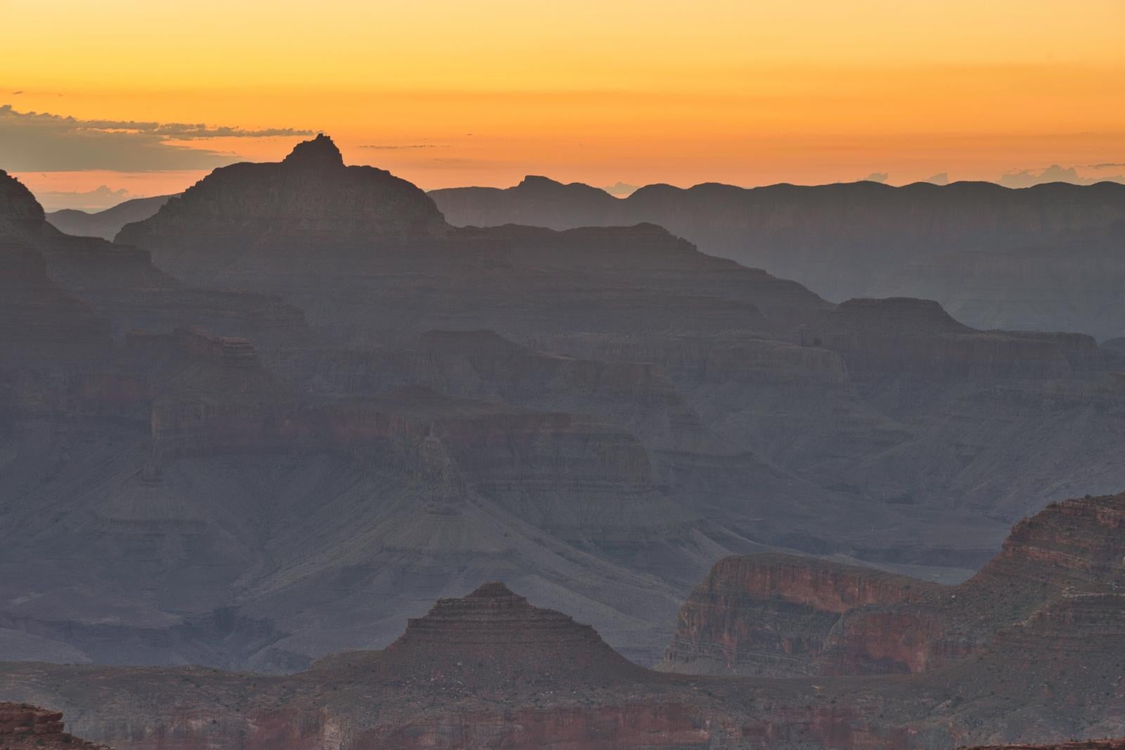 夕暮れ時のグランドキャニオン。オレンジ色の空に黒くシルエットで浮かび上がる重層的な山々と峡谷