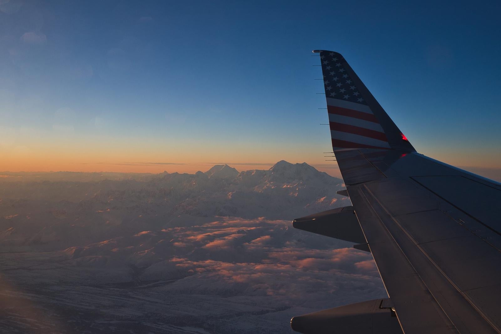 「夕日に染まる雪山と飛行機の翼の美しい風景」の写真