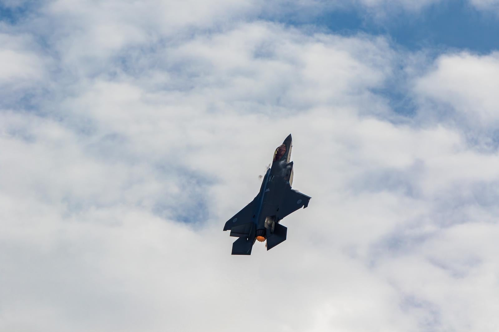 青空と雲の中をアフターバーナーで飛行する航空自衛隊の戦闘機