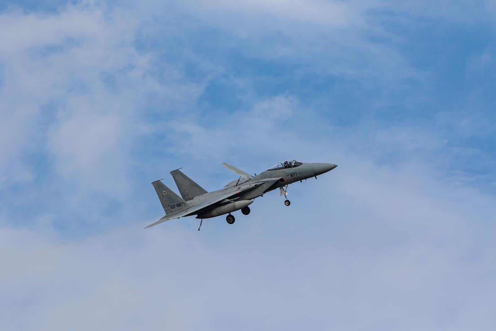 青空に白い雲が浮かぶ中を飛行する航空自衛隊の戦闘機