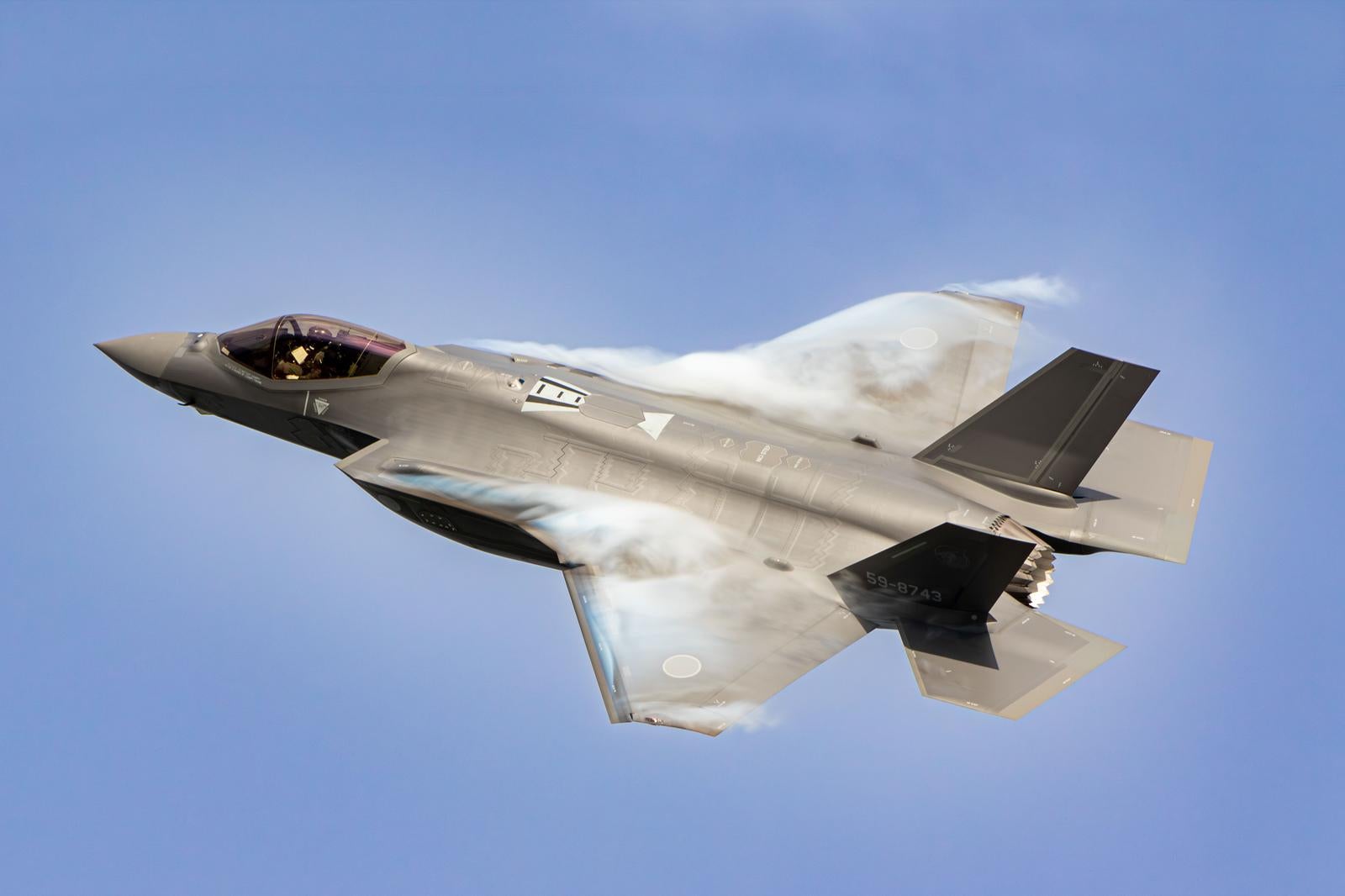 航空自衛隊の戦闘機が青空を飛行し白い気流を纏う