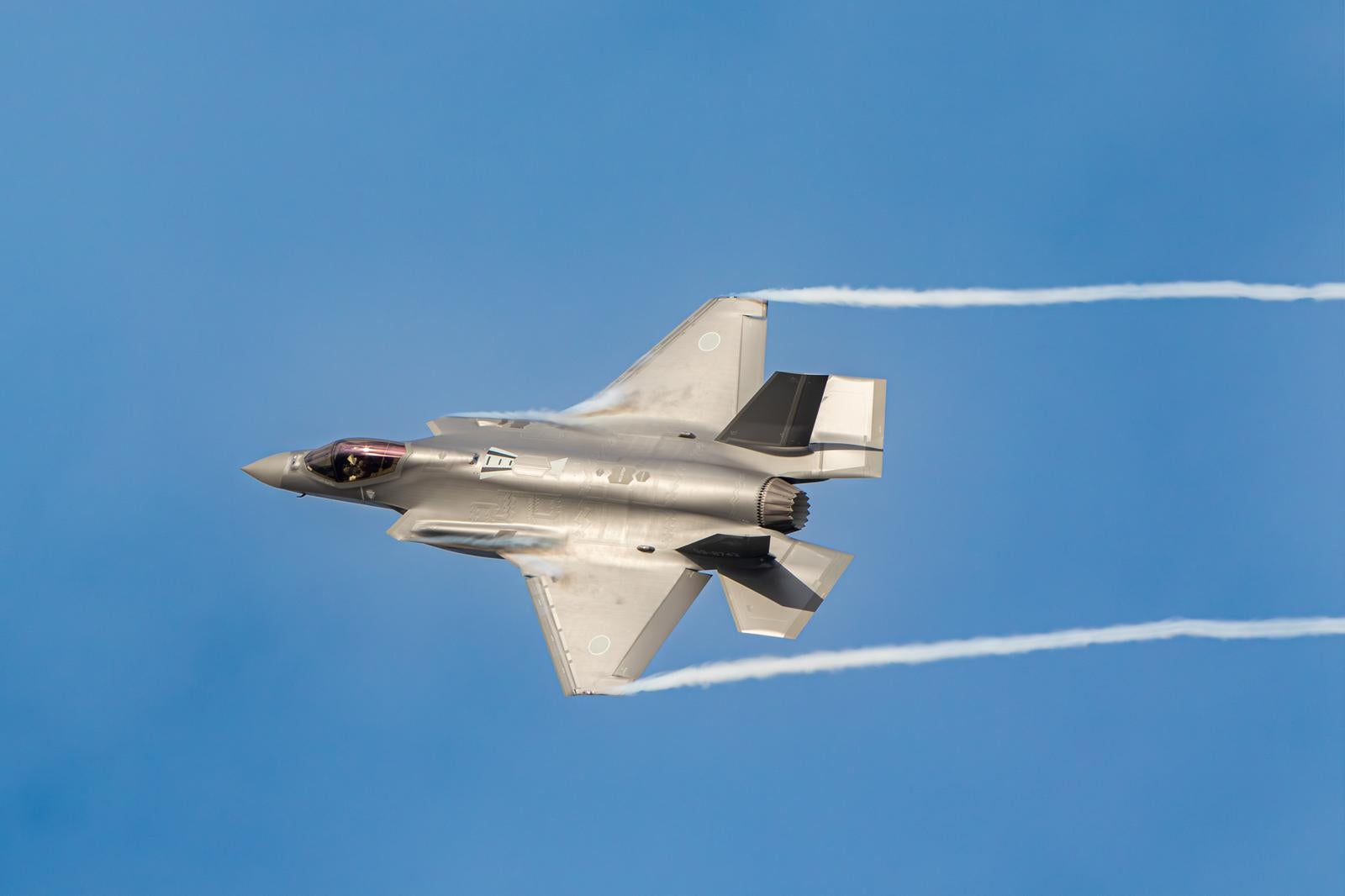 青空を高速飛行する航空自衛隊の戦闘機と白い航跡