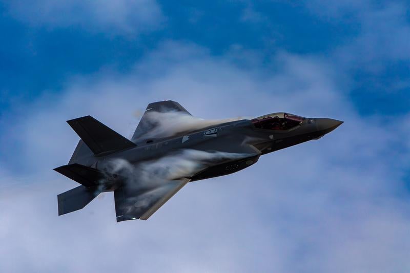 青空と雲の間を力強く飛行する航空自衛隊のステルス戦闘機F-35の写真