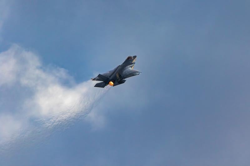青空と雲の間を飛行する航空自衛隊のステルス戦闘機F-35の写真