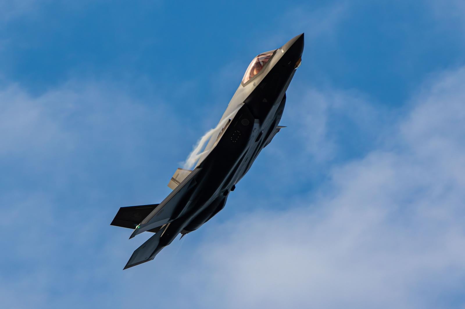 青空と雲を背景に上昇飛行する航空自衛隊のグレー色戦闘機