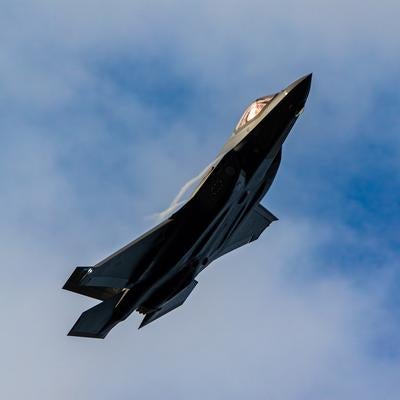 雲の浮かぶ青空を背景に力強く飛行する航空自衛隊のステルス戦闘機の写真