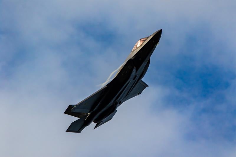 雲の浮かぶ青空を背景に力強く飛行する航空自衛隊のステルス戦闘機の写真