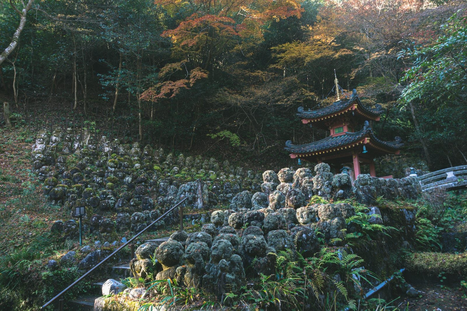 「紅葉した木々を背景に沢山の羅漢像に囲まれて建つ多宝塔」の写真