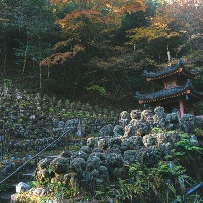 紅葉した木々を背景に沢山の羅漢像に囲まれて建つ多宝塔の写真