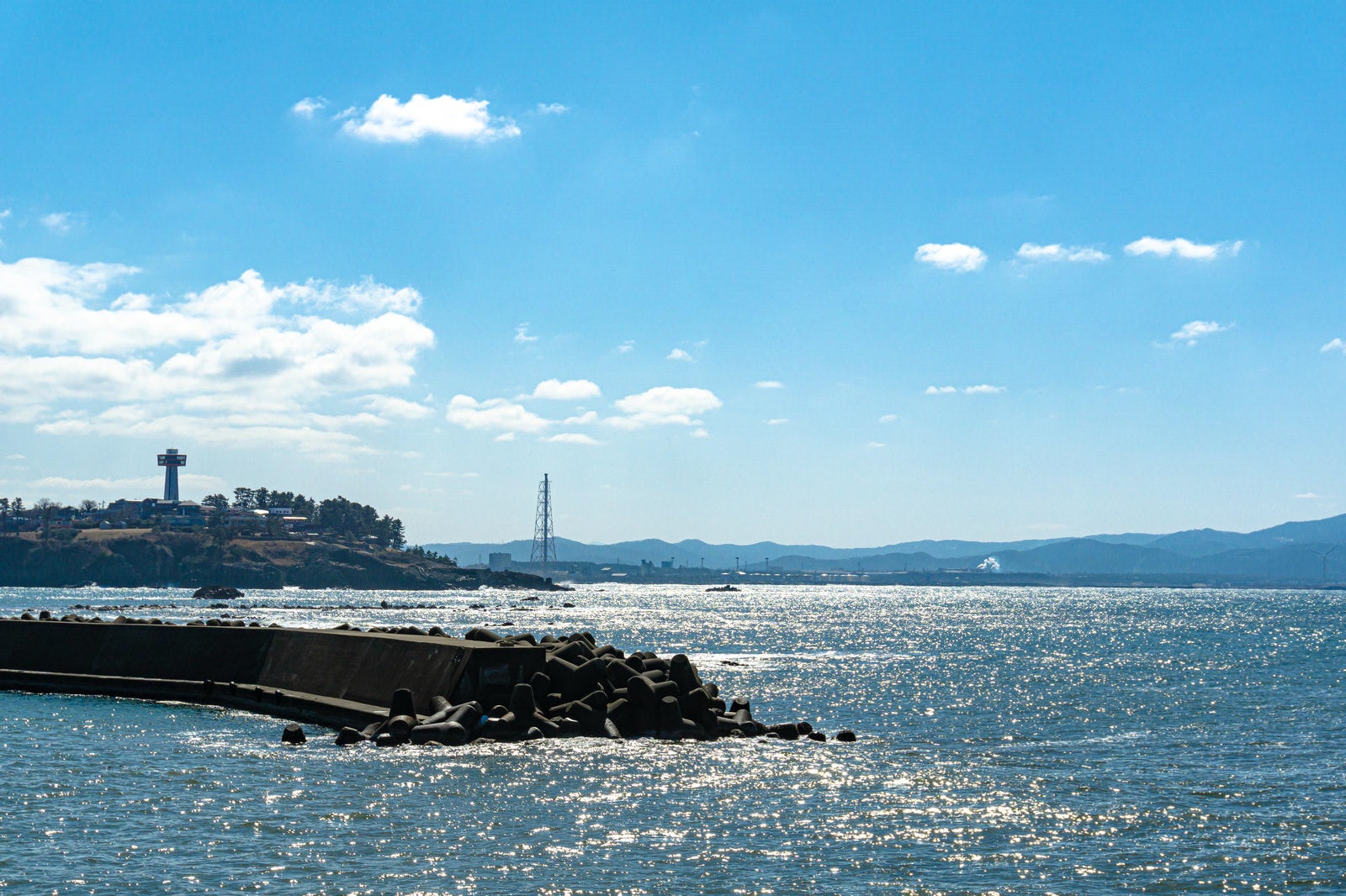 「雄島橋近くの堤防の向うに霞んで見える東尋坊や福井臨海工業地帯」の写真