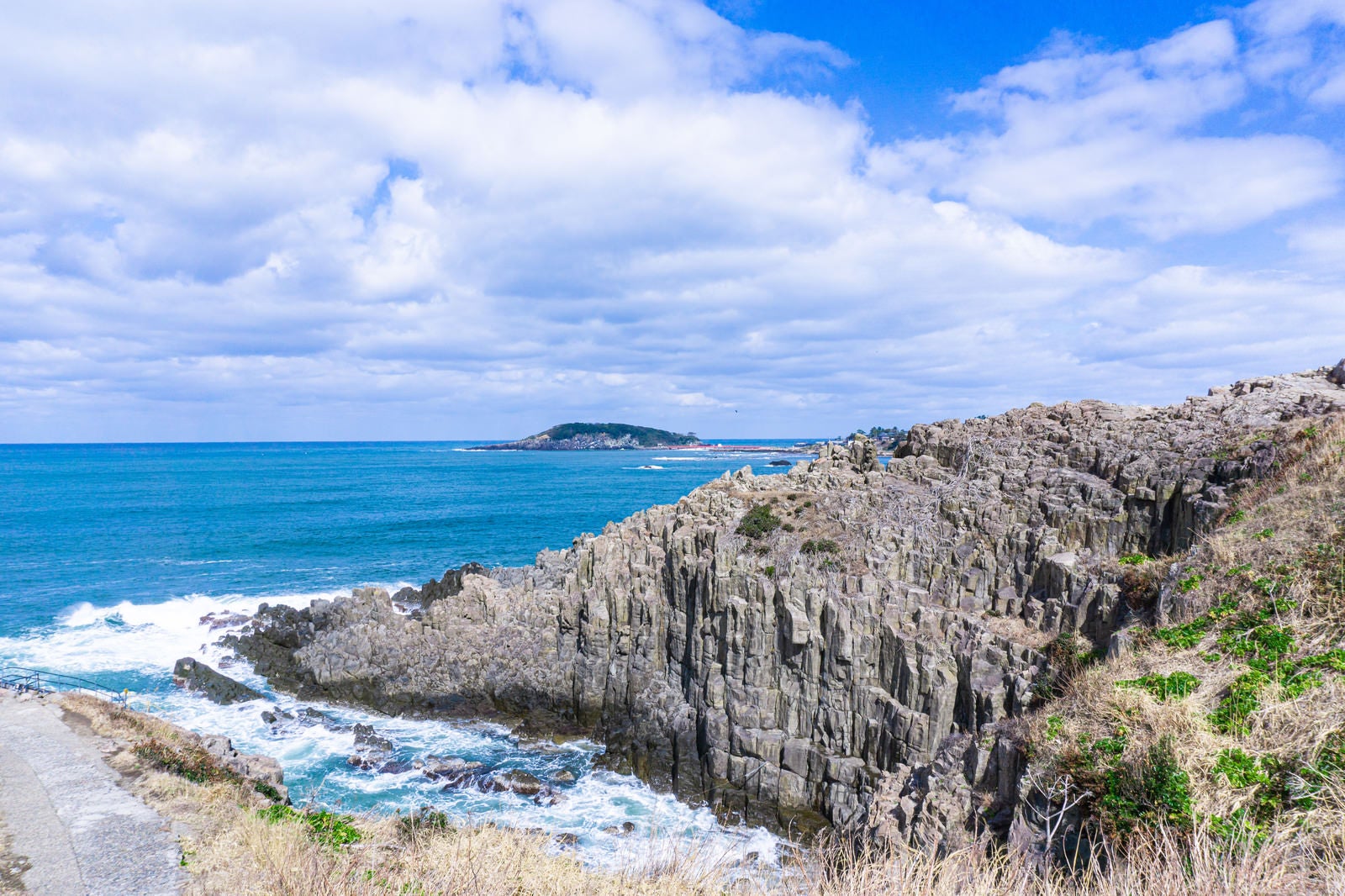 「溶岩が冷え固まった時に出来たといわれる見事な柱状節理の岩壁と雄島」の写真