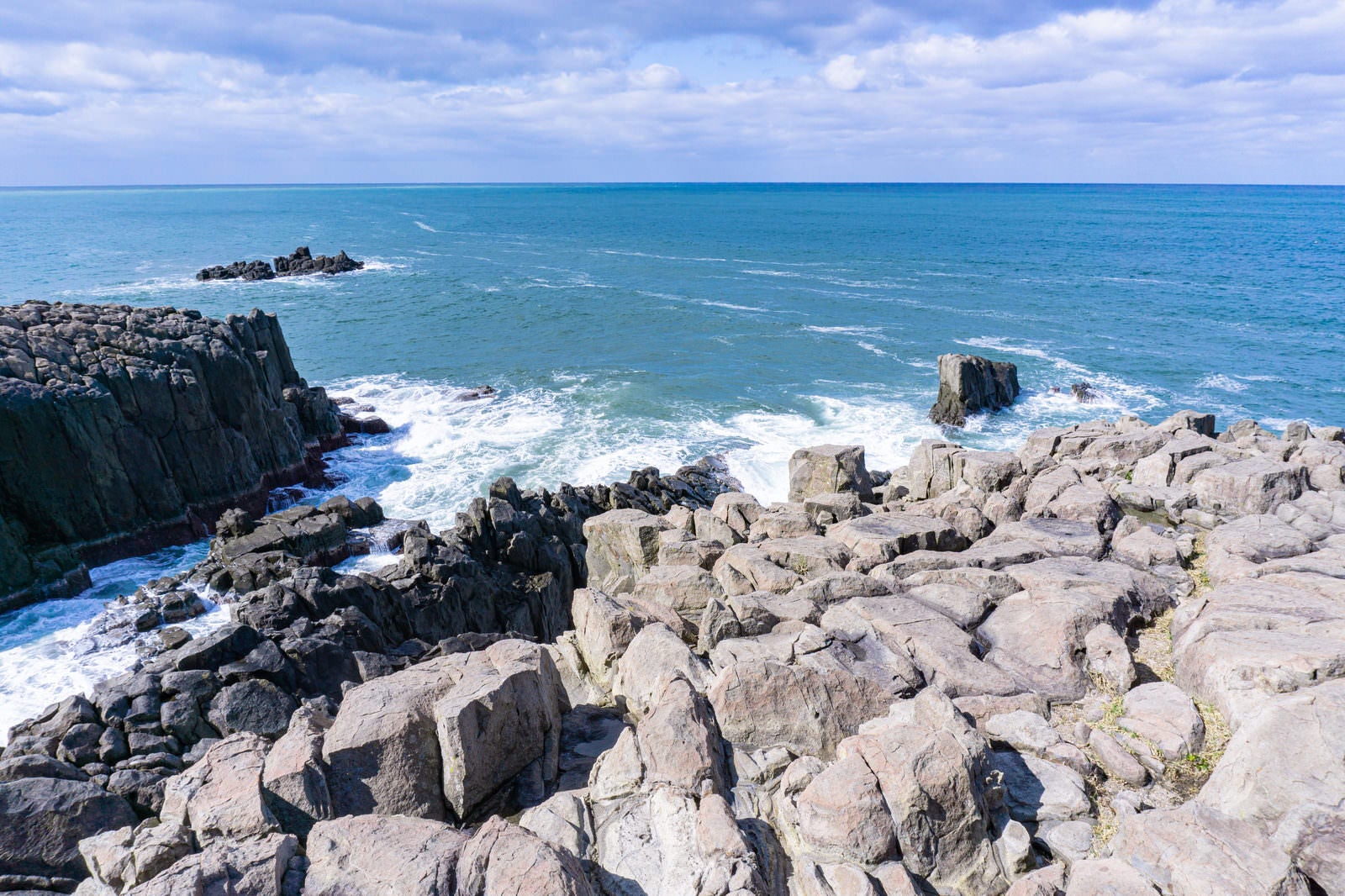 「柱状節理の特徴がわかる柱を束ねたような岩場の上部に立ち日本海を眺める」の写真