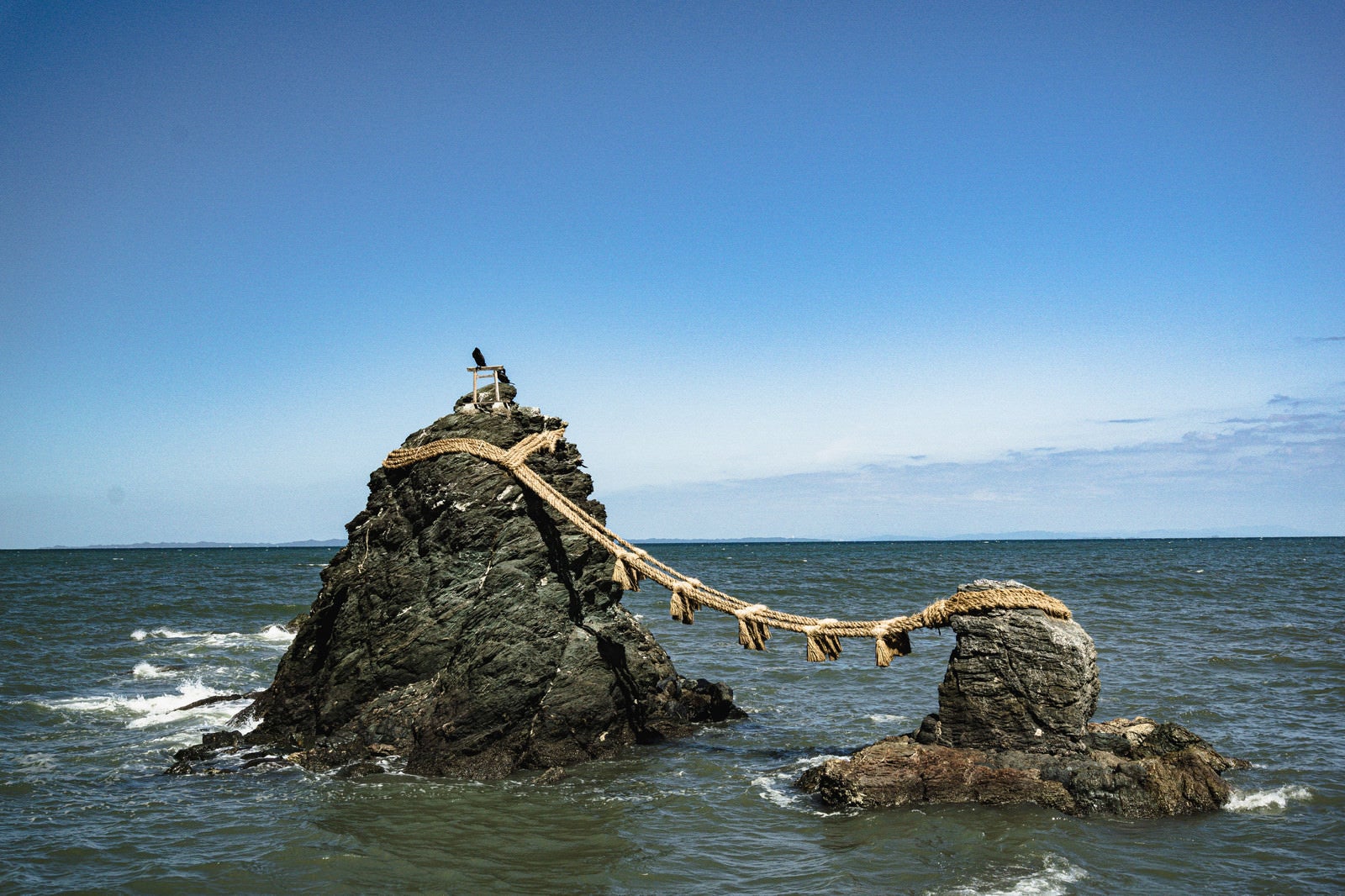 「快晴の空の下、波に打たれて立つ夫婦岩」の写真