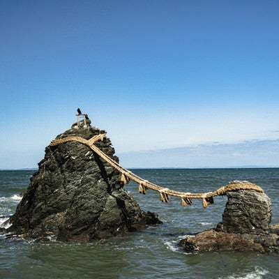 快晴の空の下、波に打たれて立つ夫婦岩の写真