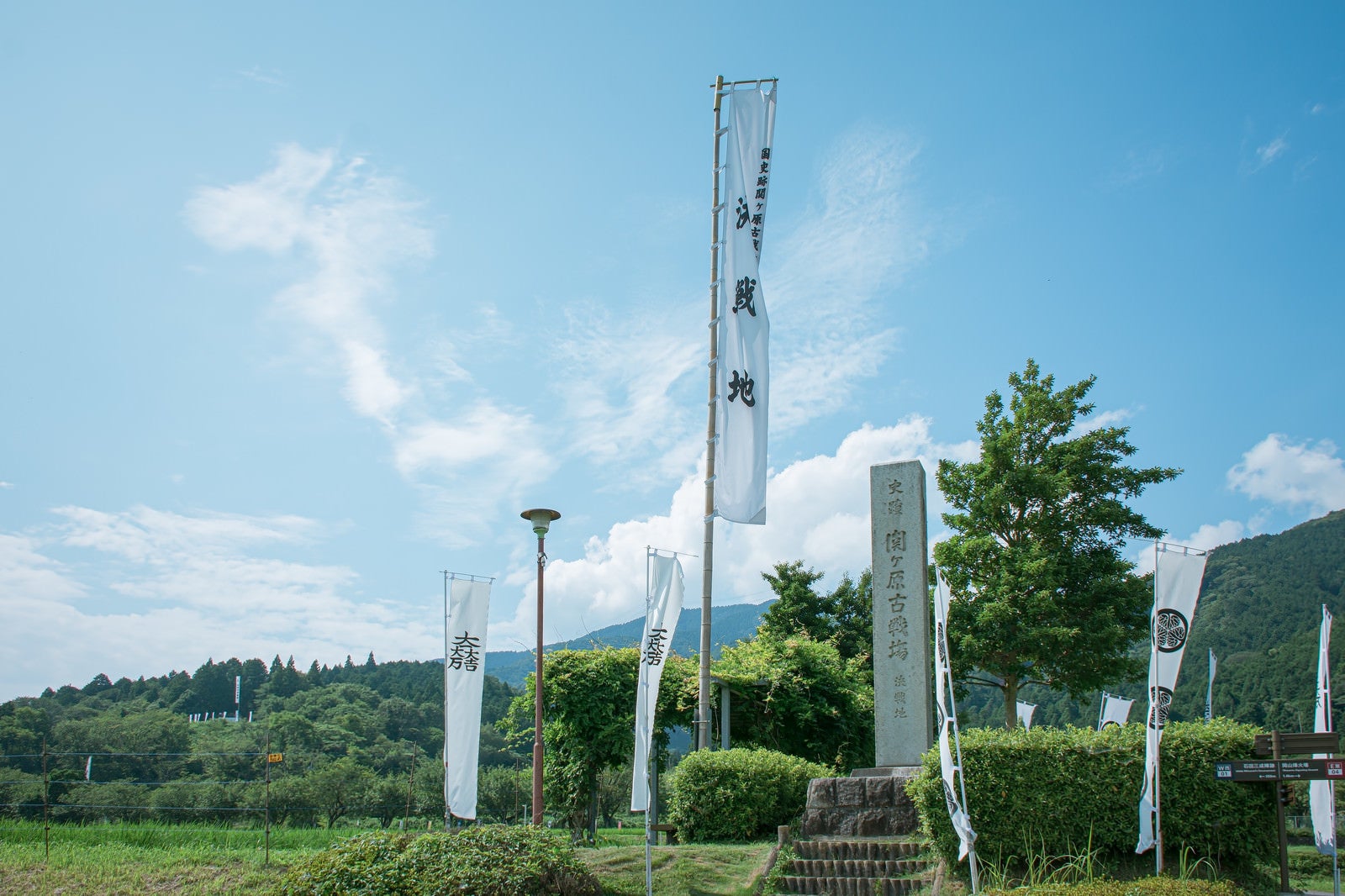 「関ケ原決戦地の石碑とその左奥に見える石田三成陣跡の展望デッキの旗印とノボリ」の写真