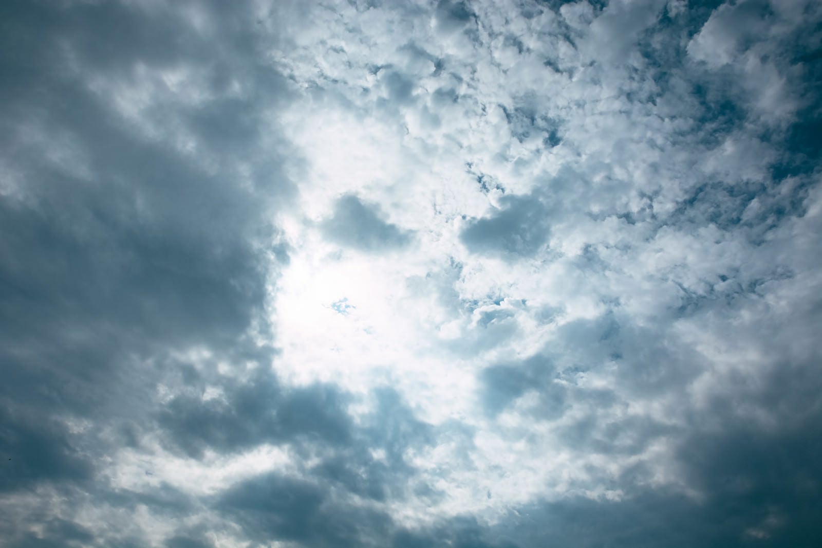 「灰色の雲の合間から光が漏れる空」の写真
