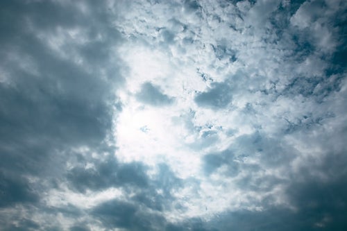 灰色の雲の合間から光が漏れる空の写真