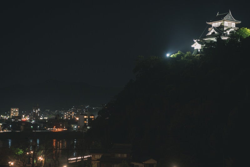 ライトアップされた犬山城と灯りを受けて輝く木曽川の向うに見える各務原市の街灯りの写真