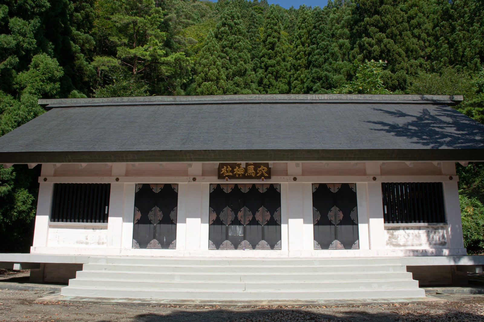 「白い壁が日に映えて美しい現代的な造りの穴馬神社（あなまじんじゃ）拝殿」の写真