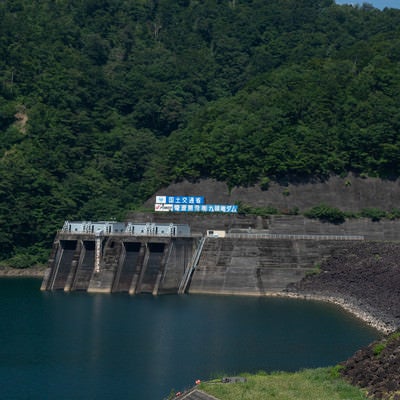 山肌に掲げられた国土交通省とダム名の看板とその下に見える発電所取水口（福井県大野市）の写真