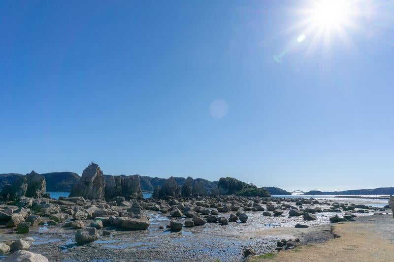 青空と太陽が輝く橋杭岩と遠くに見えるくしもと大橋の写真