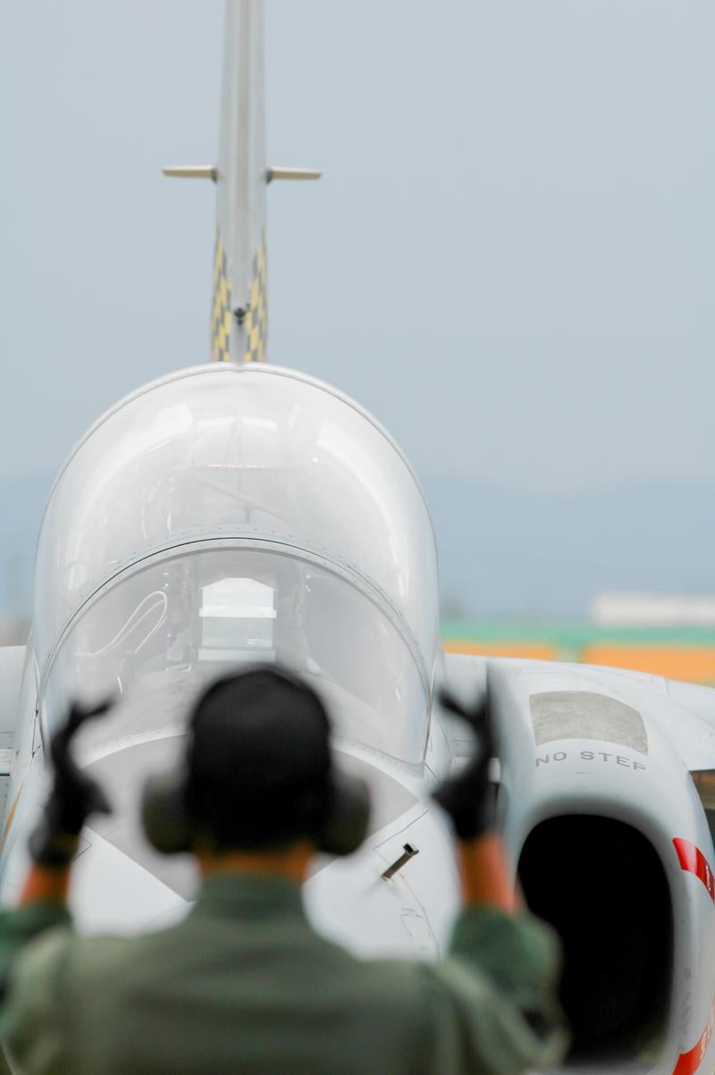 戦闘機の機首前で両手を上げて誘導する隊員の後ろ姿