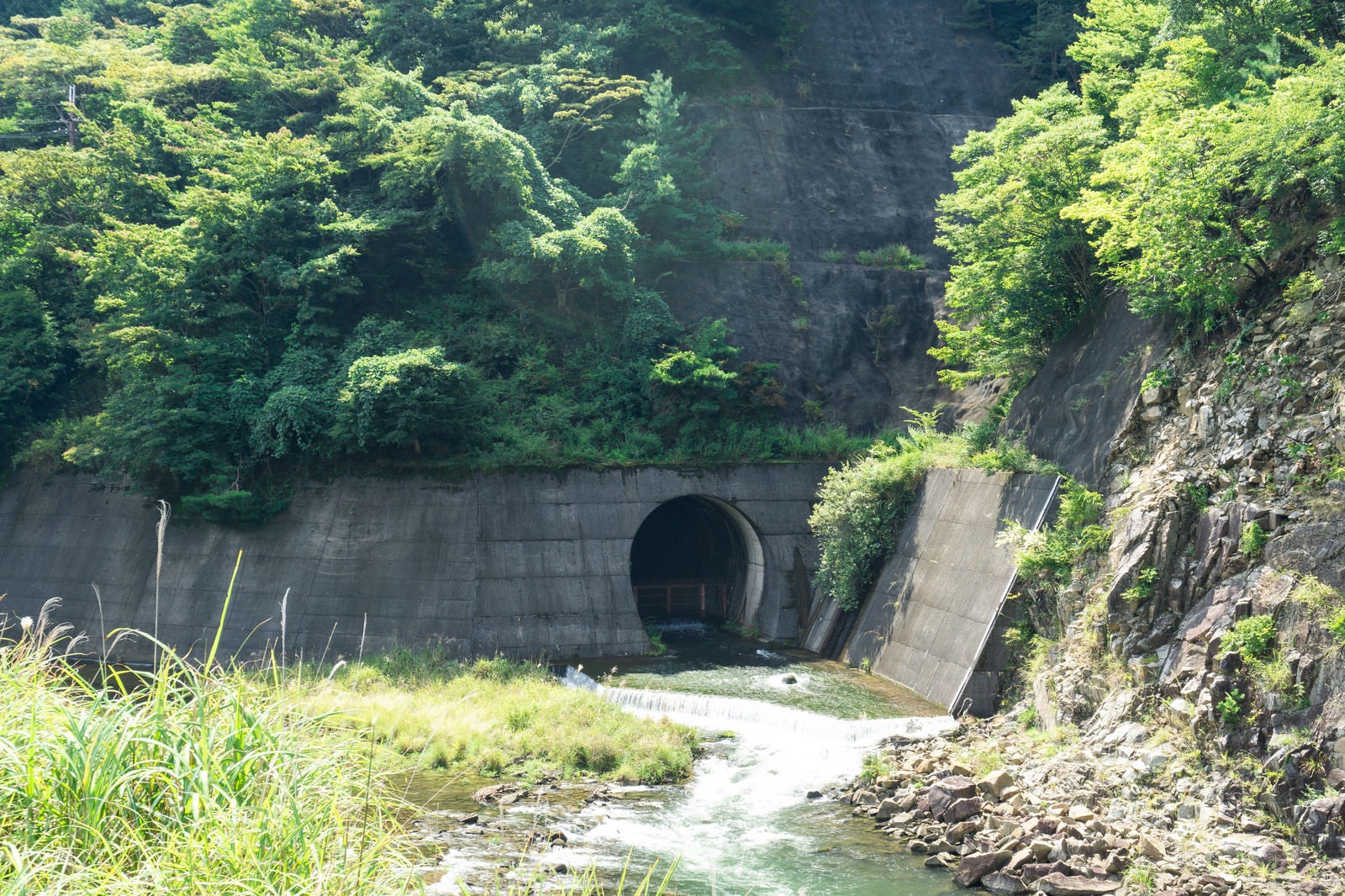 「ダム下流側の青土ダム公園から見える下流への放水口の薄暗いトンネル」の写真