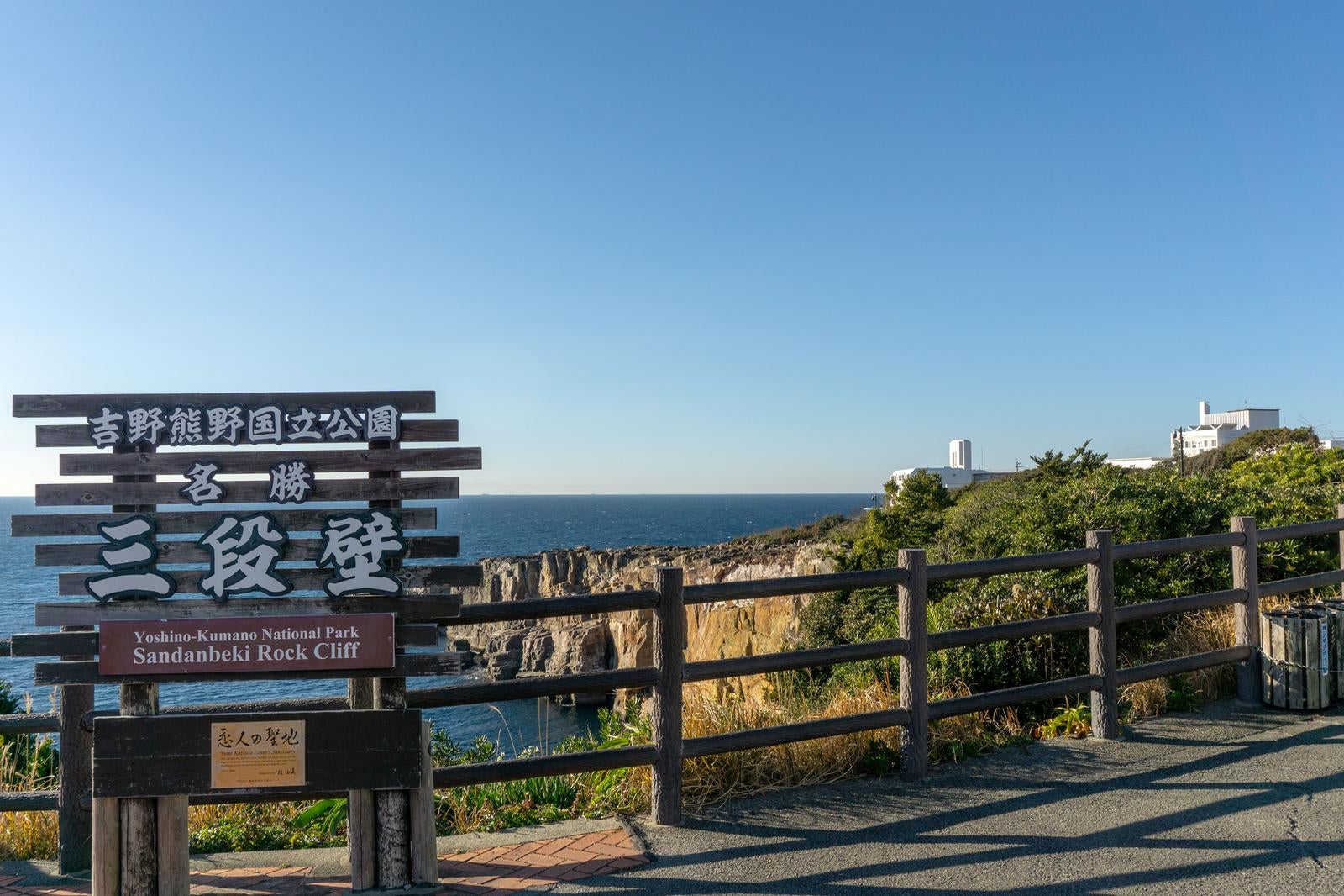 三段壁の案内板と木製手摺り越しに見る断崖と青い海
