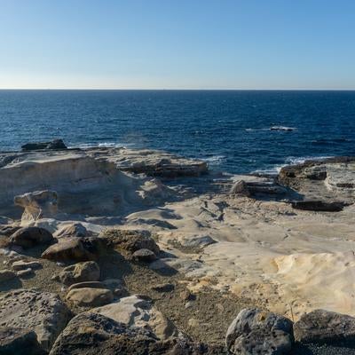 千畳敷の平らな岩盤と紺碧の海が広がる海岸線の写真