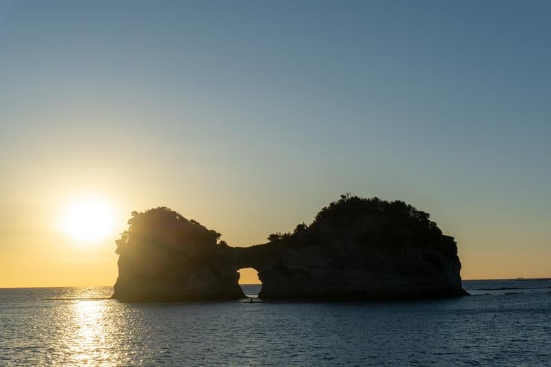 夕日に照らされる円月島と光の道の写真