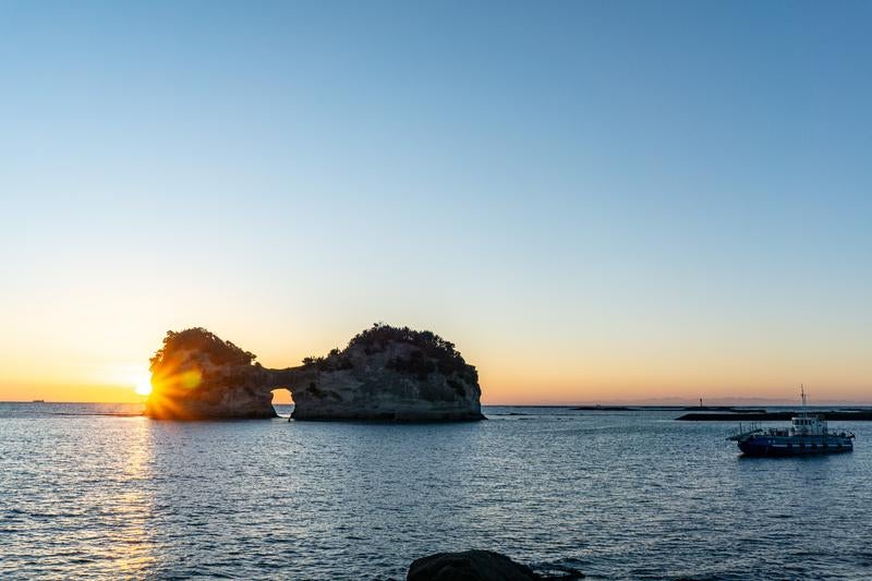 円月島の海に沈みゆく夕陽と見守るグラスボートの写真