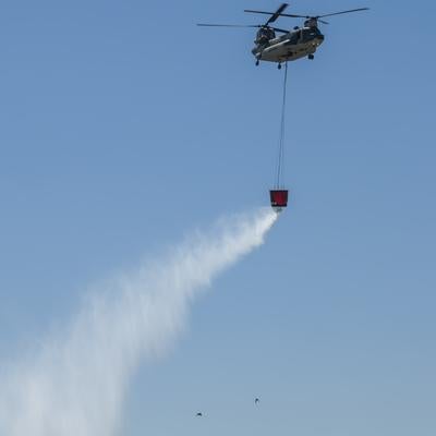 ワイヤーで吊り下げた消火バケットから放水デモを行うCH47の様子の写真