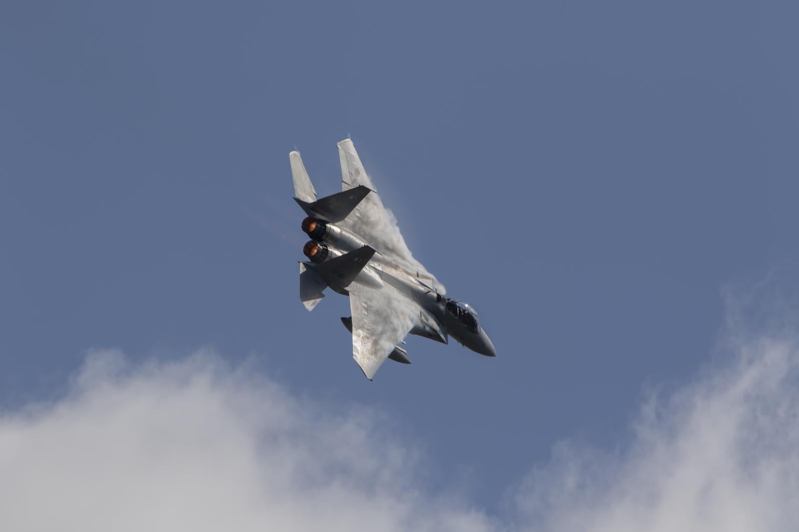 青空と白い雲を背景に飛行するグレーの戦闘機F15