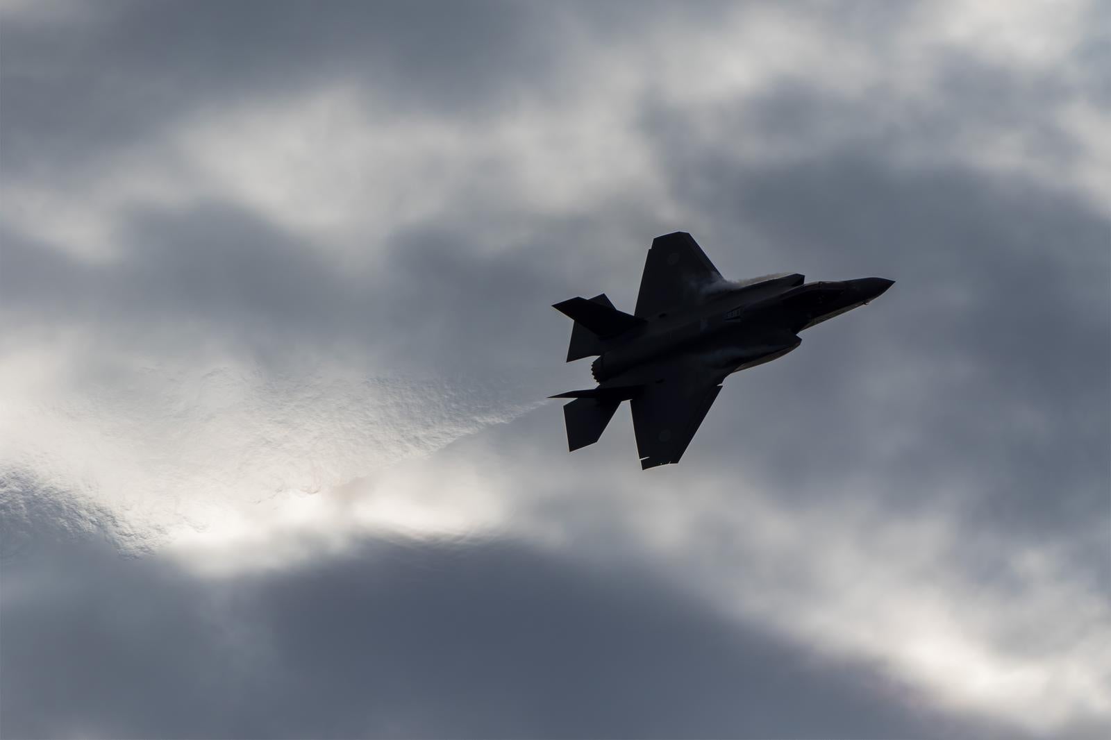 厚い雲が立ち込める曇り空を飛行するF35A戦闘機のシルエット