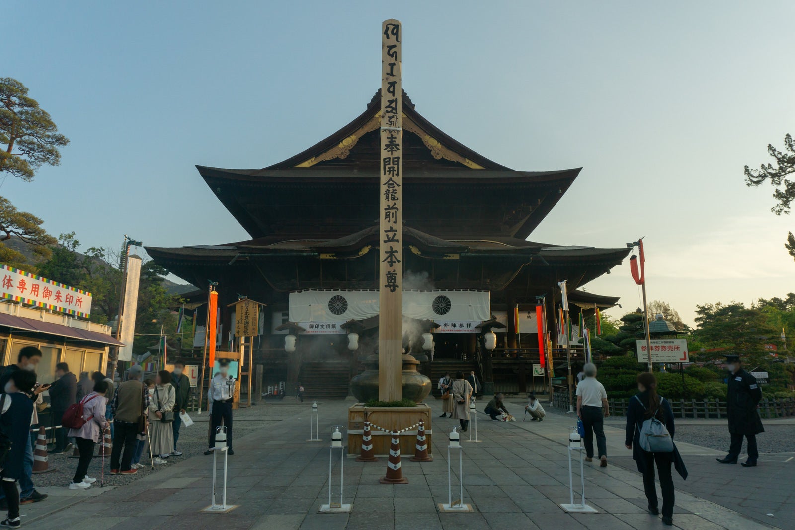 「善光寺本堂とその前に立つ約45センチ角高さ約10メートルの善光寺御開帳のシンボルとも言える回向柱」の写真